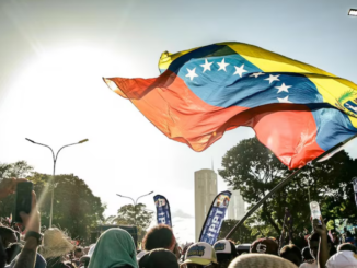 Bandeira da Venezuela tremulando acima de uma multidão durante ato público.