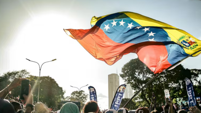 Bandeira da Venezuela tremulando acima de uma multidão durante ato público.