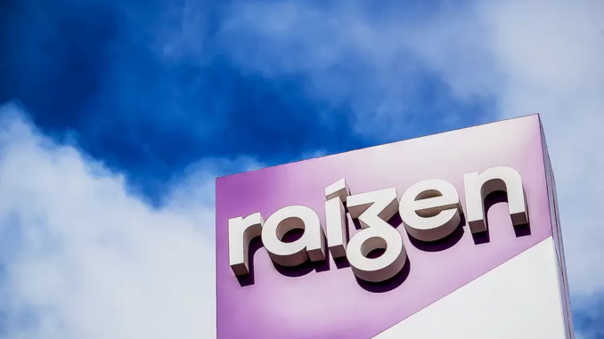 Logotipo da Raízen em destaque na fachada de um prédio com céu azul ao fundo.