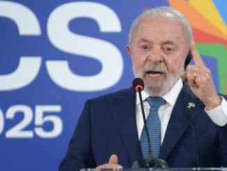 Presidente Lula discursando em púlpito, com terno azul, apontando o dedo enquanto fala diante de painel com logotipo oficial.