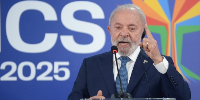 Presidente Lula discursando em púlpito, com terno azul, apontando o dedo enquanto fala diante de painel com logotipo oficial.