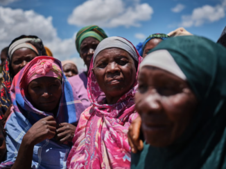 Grupo de mulheres deslocadas em Naminawe, próximo a Pemba, Moçambique, reunidas ao ar livre usando lenços coloridos, após fuga de ataques insurgentes.