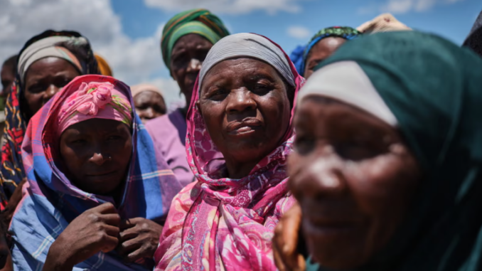 Grupo de mulheres deslocadas em Naminawe, próximo a Pemba, Moçambique, reunidas ao ar livre usando lenços coloridos, após fuga de ataques insurgentes.
