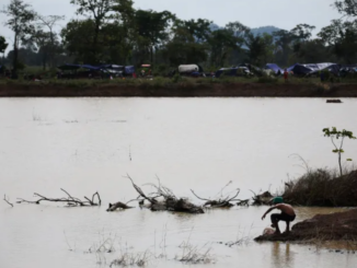 Morador cambojano próximo a lago às margens da fronteira com a Tailândia, com acampamentos ao fundo.