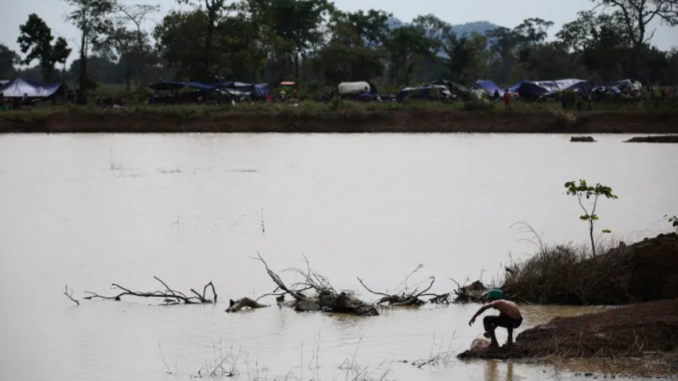 Morador cambojano próximo a lago às margens da fronteira com a Tailândia, com acampamentos ao fundo.