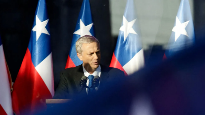 José Antonio Kast discursando em palanque com várias bandeiras do Chile ao fundo.