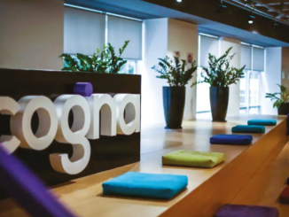 Logotipo da Cogna em área interna corporativa com plantas e ambiente moderno ao fundo.