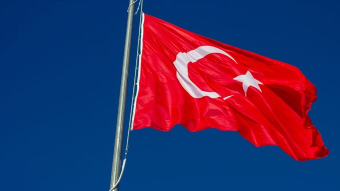 Bandeira da Turquia tremulando em mastro contra o céu azul.