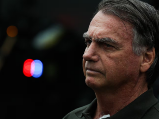 Ex-presidente Jair Bolsonaro com expressão séria em ambiente externo, com luzes desfocadas ao fundo