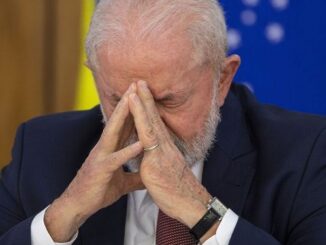 Presidente Luiz Inácio Lula da Silva com mãos unidas no rosto em expressão séria durante cerimônia oficial.