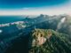 Vista aérea do Cristo Redentor no Rio de Janeiro, com montanhas, mar e cidade ao fundo em dia ensolarado.