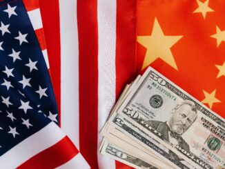 Bandeiras dos Estados Unidos e da China lado a lado com cédulas de dólares à frente, representando tensões econômicas e comerciais.