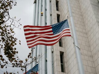 Bandeira dos Estados Unidos tremulando em mastro diante de prédio governamental.