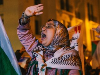 Mulher com hijab segurando bandeira e protestando em apoio à Palestina durante manifestação noturna.