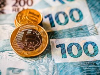 Notas de 100 reais com duas moedas de 1 real simbolizando o reajuste do salário mínimo em 2026