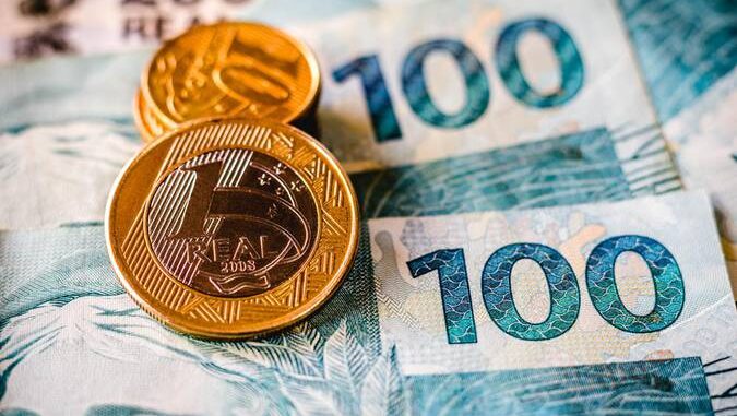 Notas de 100 reais com duas moedas de 1 real simbolizando o reajuste do salário mínimo em 2026