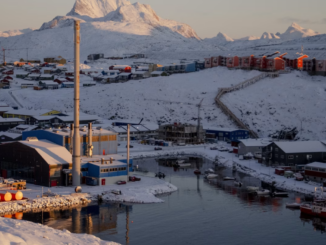 Cidade costeira da Groenlândia coberta de neve, com instalações industriais, porto marítimo e montanhas ao fundo em cenário ártico estratégico