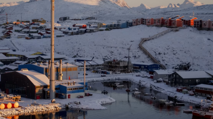 Cidade costeira da Groenlândia coberta de neve, com instalações industriais, porto marítimo e montanhas ao fundo em cenário ártico estratégico