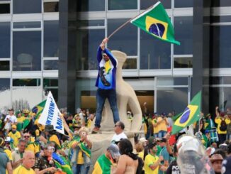 Manifestantes invadem a Praça dos Três Poderes em Brasília durante os ataques de 8 de janeiro de 2023, segurando bandeiras do Brasil em frente ao Congresso Nacional.