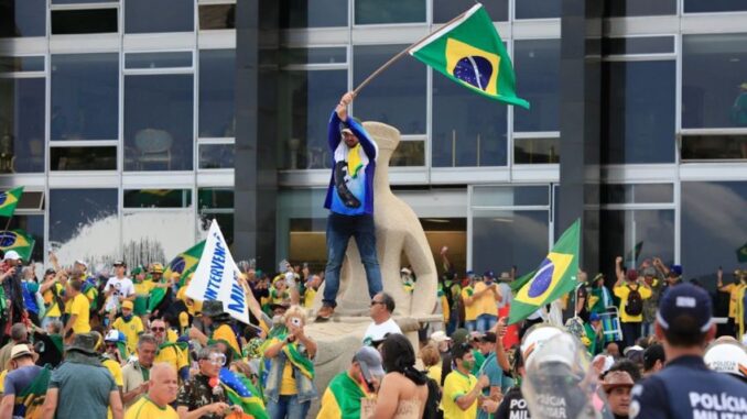 Manifestantes invadem a Praça dos Três Poderes em Brasília durante os ataques de 8 de janeiro de 2023, segurando bandeiras do Brasil em frente ao Congresso Nacional.